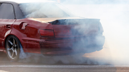 A red car is driving with smoke coming out of the back