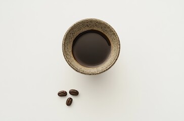 Elegant Flat Lay of a Dark Brewed Coffee in a Textured Ceramic Cup with Coffee Beans on a Soft Background