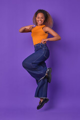 Young African American woman is joyfully jumping in mid-air, showcasing her colorful outfit.