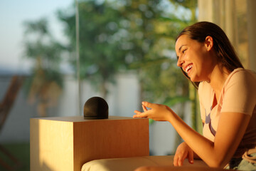 Happy woman talking to smart speaker at sunset
