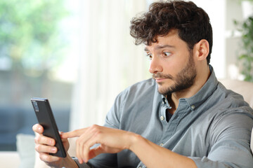Perplexed man checking cell phone at home