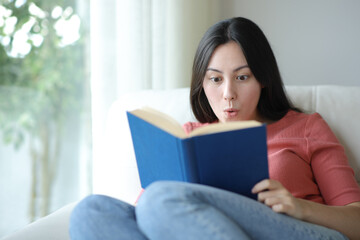 Amazed asian woman reading a book on a couch
