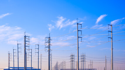 Row of many electric poles with cable lines in industrial settlement area against blue sky background