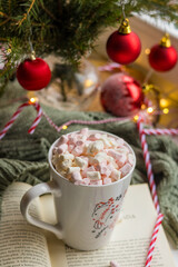 Cup of hot cocoa with marshmallow and cinnamon stick surrounded by spruce branches. Cozy seasonal holidays