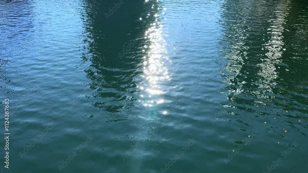 Poster sunlight reflecting on calm water with rippling patterns and a serene urban backdrop