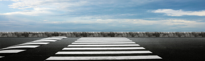 Asphalt street with pedestrian crosswalk and blue sky with clouds in the background