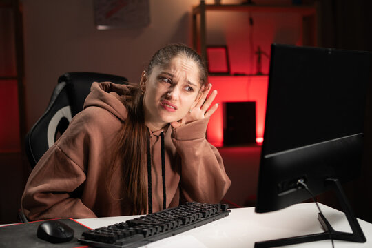 Portrait of female gamer in hoodie, with hand over ear listening sitting in a room with red light