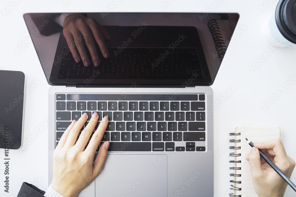 Poster detailed view of a woman's hand jotting down notes in a notepad on a modern laptop, with a blurred b