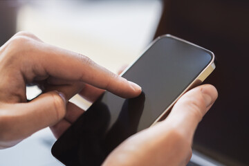 Woman busily working on her state-of-the-art smartphone, laptop waiting in the background within the blurry contours of a contemporary office space