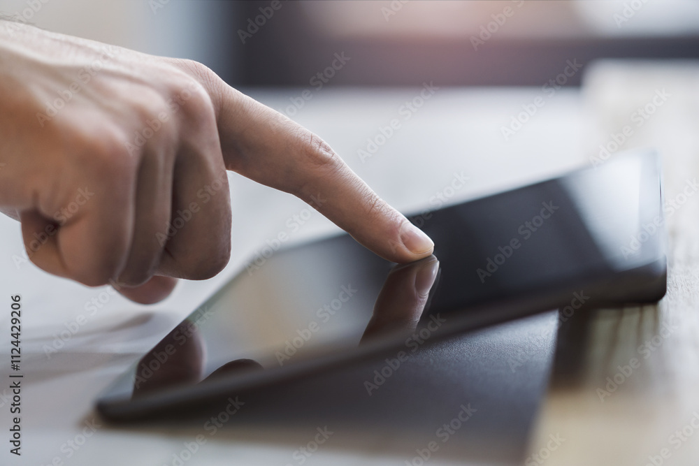 Poster closeup view of a male finger operating a high-tech tablet on a desk, set against the blurred backdr