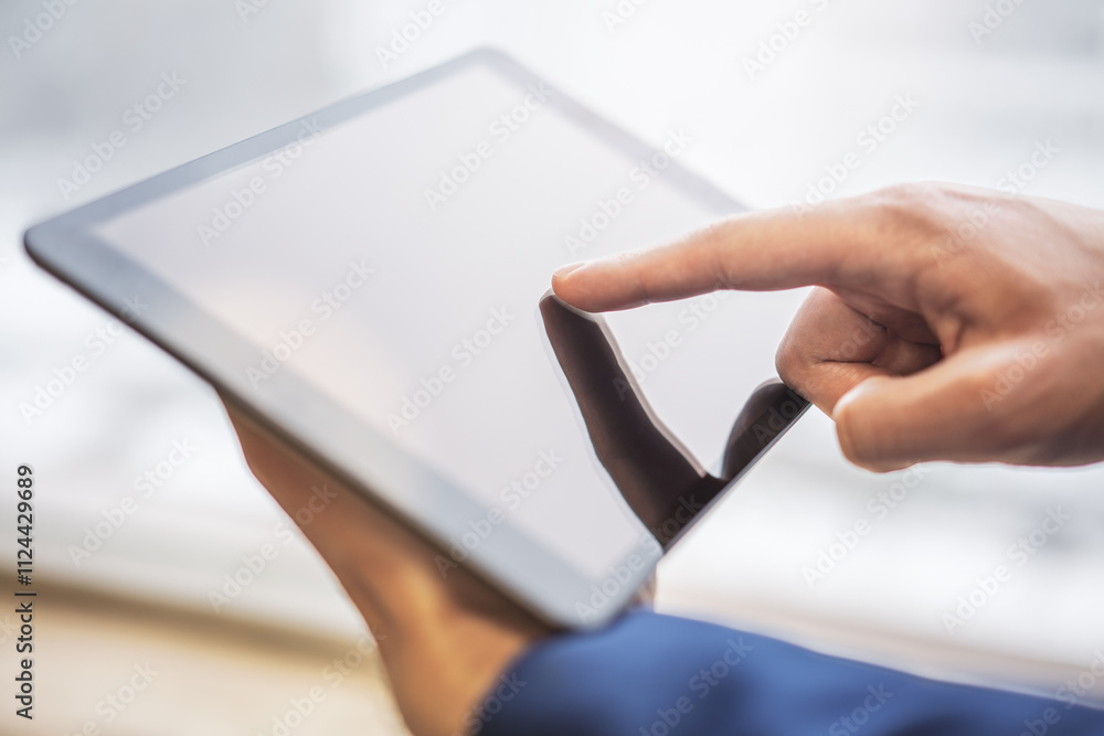 Poster man's hand operating a modern tablet device placed on a desk, surrounded by the blurry contours of a