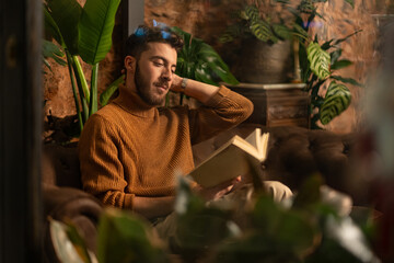 Relaxed young man enjoying book in atmospheric cafe surrounded by plants