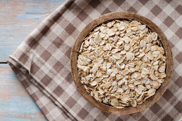 Wooden Bowl with Dry Oatmeal on Checkered Linen Napkin, Top View