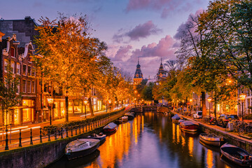 As twilight descends on Amsterdam, the charming canals reflect the golden hues of autumn trees. Shops glow warmly while boats float serenely, Christmas in Amsterdam with street lights