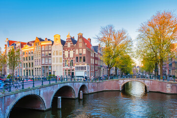 Golden leaves flutter in the crisp autumn breeze as cyclists traverse peaceful bridges in Amsterdam Keizersgracht, surrounded by charming canal houses 
