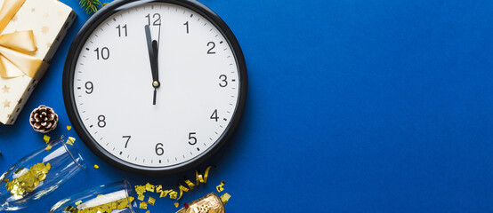 New year celebration concept with a bottle of champagne and two glasses toasting. Christmas gift box, alarm clock and fir tree branch on colored table. Top view Copy space