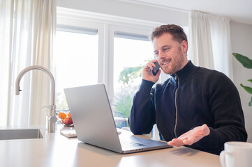 Fototapeta premium working at home in the kitchen. caucasian male sitting at the kitchen counter behind his laptop working and communicating.