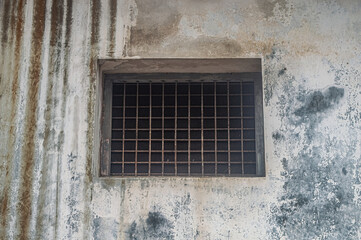 Old, weathered concrete wall with a barred window. The wall shows signs of decay and discoloration, adding a rustic and abandoned feel to the scene