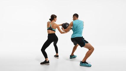 Sportive couple, young man and woman in sportswear training together, doing exercises with medicine ball against white studio background. Sport, active and healthy lifestyle, workout, fitness concept