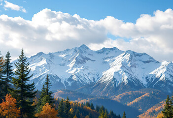 Fototapeta premium A snowy mountain range with pine trees and fall foliage in the foreground, set against a blue sky with fluffy white clouds