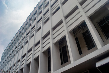 Fototapeta premium A modern, multi story building with a unique geometric facade featuring rectangular windows and concrete patterns, captured from a low angle against a cloudy sky