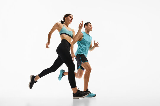 Low angle side view image of young athletic woman and muscular man in motion, training, running against white studio background. Concept of sport, active and healthy lifestyle, workout, fitness