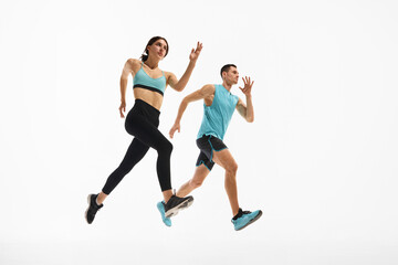 Low angle side view dynamic image of young athletic woman and muscular man in motion, training, running against white studio background. Sport, active and healthy lifestyle, workout, fitness concept