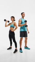 Full-length image of young woman and man with fit, sportive,strong bodies, standing with dumbbell...