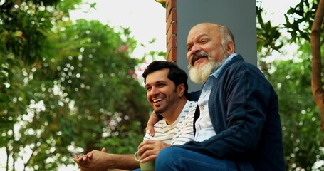Indian Asian Happy Old Aged Father and Young Adult Son Sitting on Porch of Home Outdoors, Engaging in Heartfelt Conversation and Laughing Together, Showcasing Father-Son Bonding