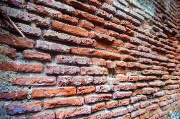 A close up of an old, weathered brick wall with uneven, rough textured red bricks and visible mortar, showcasing rustic charm and historical architecture