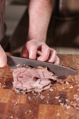 Male hands cutting cooked meat beef on a wooden board