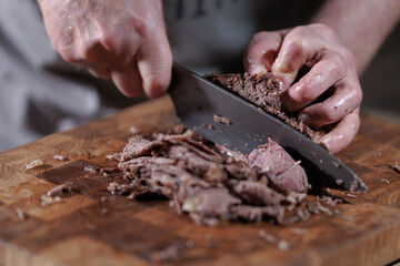 Male hands cutting cooked meat beef on a wooden board