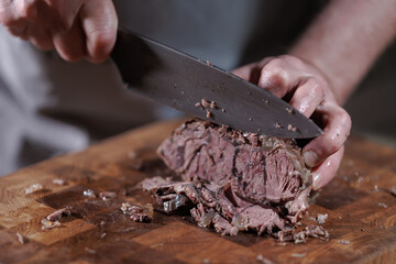 Male hands cutting cooked meat beef on a wooden board