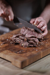 Male hands cutting cooked meat beef on a wooden board