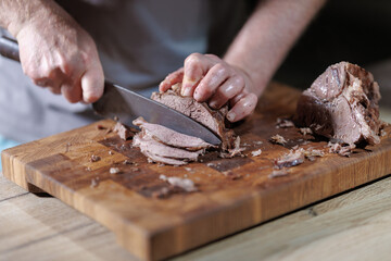 Male hands cutting cooked meat beef on a wooden board