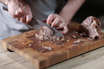 Male hands cutting cooked meat beef on a wooden board