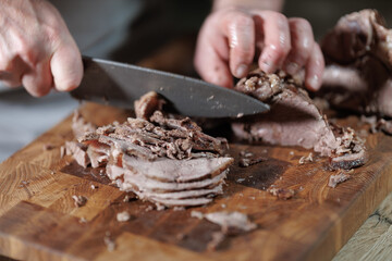Male hands cutting cooked meat beef on a wooden board