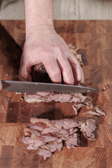 Male hands cutting cooked meat beef on a wooden board