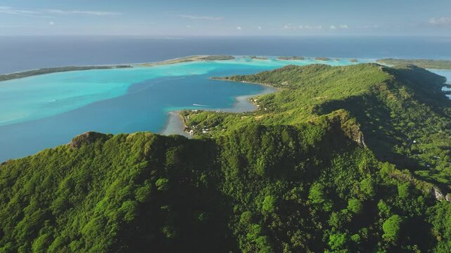 Aerial drone footage captures the breathtaking beauty of Bora Bora mountains, tropical island in French Polynesia, where lush green vegetation covers volcanic slopes meeting a vibrant turquoise lagoon