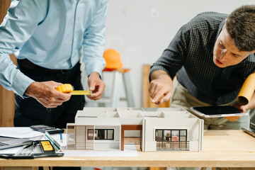 Professional collaboration in architecture. Two engineers work on construction plans, using tools like laptops, tablets, and scale models.