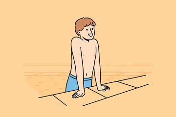 Boy gets out of pool and smiles after swimming in water, and rejoices at visiting aquapark. Happy child in swimming pool for sports training or summer recreation to improve health and get tan