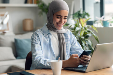 Happy freelancer using mobile phone near laptop at desk