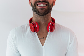 Happy cropped unrecognizable male with beard listening to music in red wireless headphones while...