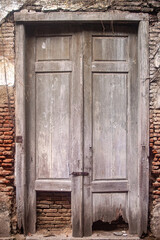 An old, weathered wooden door with peeling paint and visible damage at the bottom, set in a brick wall, showcasing the passage of time