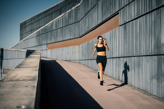 Active young woman running near wall on sunny day
