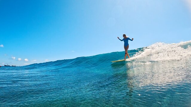 Young athletic woman in a blue swimsuit is riding a yellow surfboard on ocean waves. Maldives