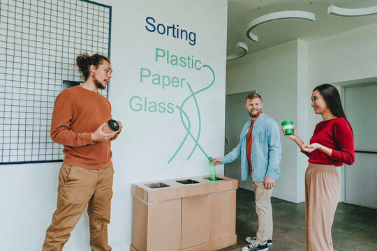 Happy business people throwing plastic bottle and coffee cups in garbage bin at office