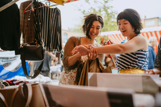 Two young women shopping at a flea market outdoors during the daytime.