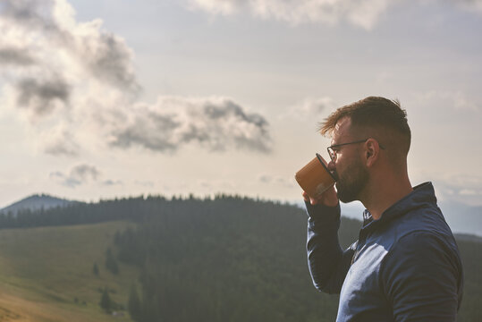 Handsome bearded man Enjoying Hot Drink with Scenic Mountain View - Powered by Adobe