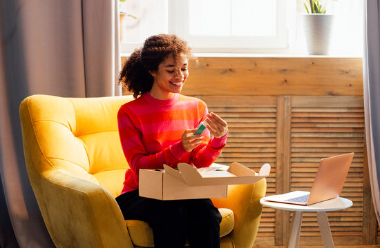 A young attractive African woman in casual clothing is unpacking a beauty box with cosmetic products